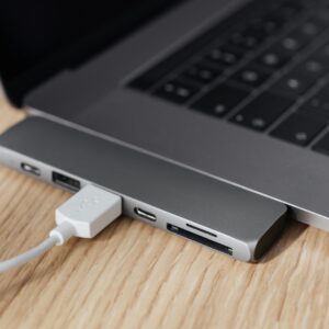 High angle of modern space silver laptop with USB type c multiport hub with plugged white cable placed on wooden table